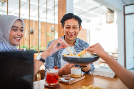 young Asian man smiling while enjoying a snack with friends at a coffee shopの写真素材