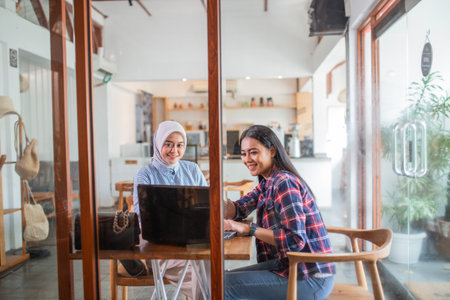 two women sit using a laptop computer working together at a coffee shopの写真素材