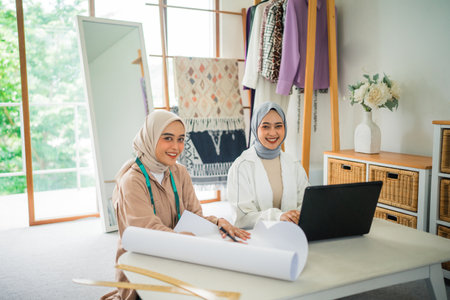 two smiling Muslim designer women working together with a laptop in a workshopの写真素材