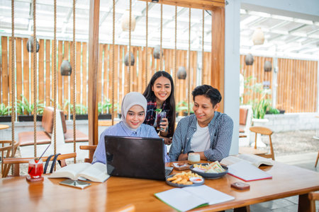 three university students use and look at a laptop together at a coffee shopの写真素材