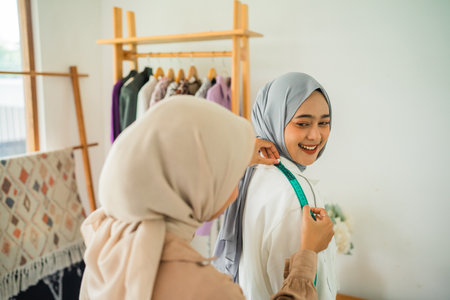 Two women wearing beautiful hijabs are busy preparing stylish outfits in a chic boutique settingの写真素材