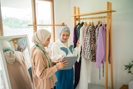 female customer in hijab chooses clothes on the shelf with a Muslim designer at a workshopの写真素材