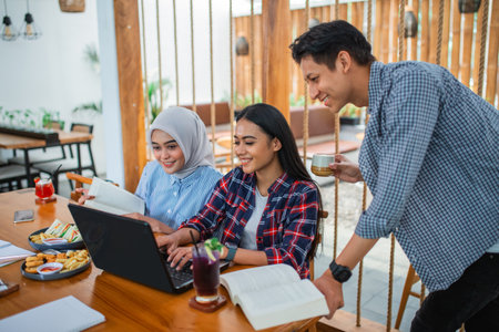 Group of Asian students studying together on a laptop while enjoying a drink at a coffee shopの写真素材