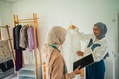 Two women discuss fashion trends at a chic studio, surrounded by stylish outfitsの写真素材