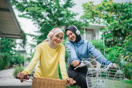 two beautiful Muslim women wearing headphones on a morning bike ride in the parkの写真素材