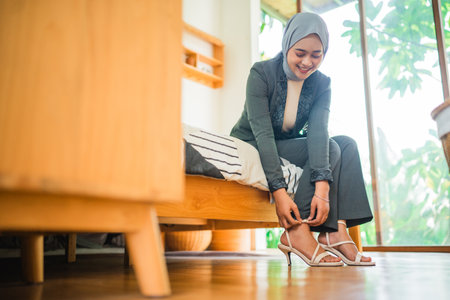 Muslim woman office worker in hijab wearing shoes getting ready before work in a roomの写真素材