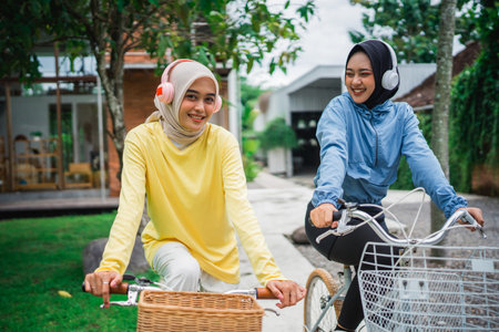 young veiled woman with headphones on a bicycle with friends cycling in front of the houseの写真素材