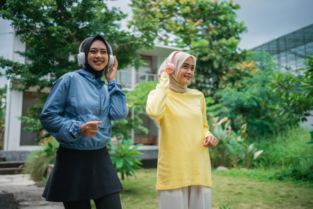 two Muslim women wearing headphones enjoy music by dancing while exercising outdoorsの写真素材