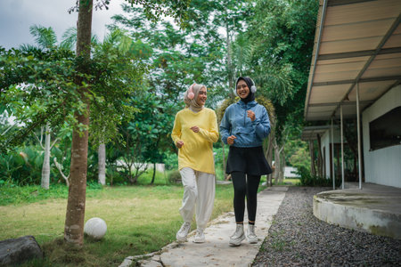 young veiled woman with headphones jogging with friends on a path in the parkの写真素材