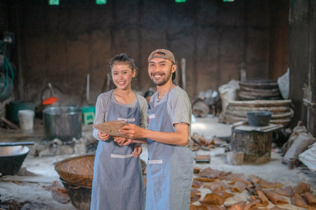 Two smiling artisans proudly display their beautiful handmade creations in a charming workshopの写真素材