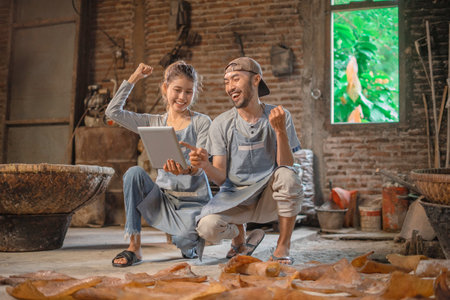 Happy artisans rejoicing over their creative success with digital tools in a rustic environment.の写真素材