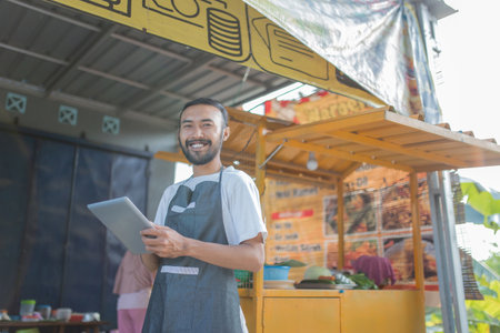 A cheerful vendor skillfully uses a tablet at a vibrant outdoor food stall, attracting customersの写真素材