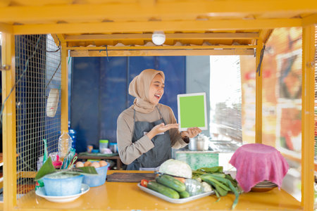A young woman in a food stall holding a blank green sign, surrounded by fresh produce.の写真素材