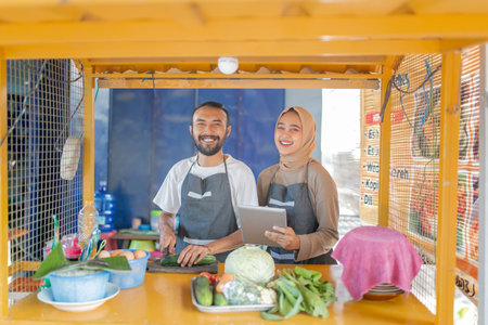 A joyful couple passionately serving fresh and highquality ingredients in their vibrant food stallの写真素材