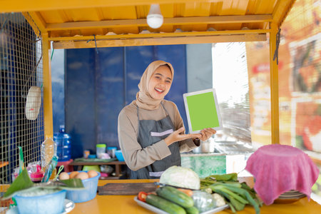 A cheerful woman is standing at a vibrant market stall, holding a bright green sign highの写真素材