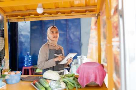 A cheerful vendor showcases fresh vegetables in a colorful market stall, attracting customersの写真素材