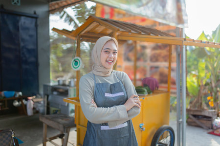 A young woman stands confidently beside a colorful food cart in a vibrant outdoor market.の写真素材