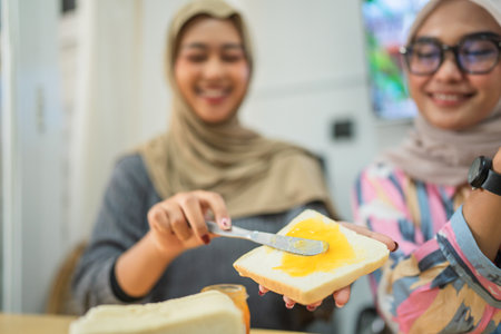 Two friends joyfully spread creamy butter on fresh bread in a warm, laughterfilled kitchenの写真素材