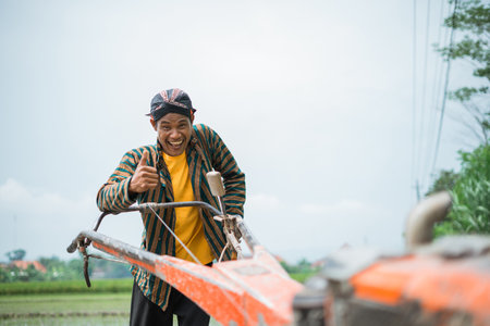 A cheerful farmer engages in plowing the vibrant, lush rice paddies beneath a cloudy skyの写真素材