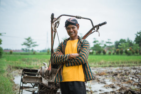 A happy and joyful farmer joyfully poses with his plow in a lush, vibrant rice fieldの写真素材