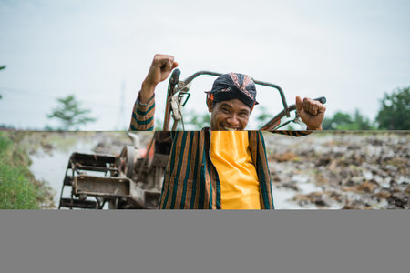 A cheerful and happy farmer joyfully poses with his tools in a vibrant green rice field