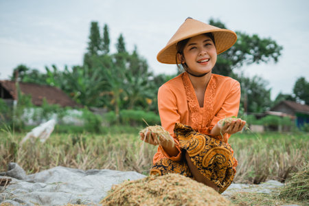 A smiling young farmer joyfully celebrates the successful rice harvest in a vibrant fieldの写真素材