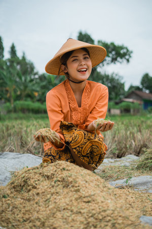 A joyful farmer, dressed in traditional clothing, gathers ripe rice beneath a clear blue skyの写真素材