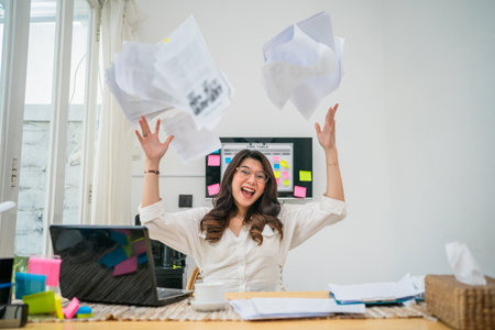 A joyful woman celebrates her success by tossing papers in an office, radiating positivityの写真素材
