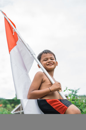 handsome boy smiling shirtless carrying red and white flag during Indonesian independence celebration with white sky backgroundの写真素材