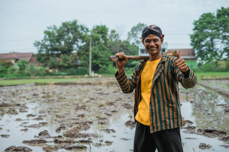 A joyful and happy farmer stands proudly while holding a tool in a rice fieldの写真素材