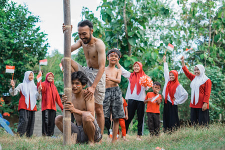 two shirtless adult men take part in pinang climbing to celebrate Indonesian independenceの写真素材