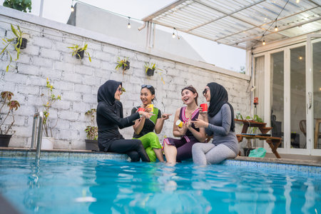 Women are laughing and relaxing by the pool with colorful drinks on a sunny summer day