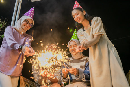Friends gather joyfully, celebrating under a festive atmosphere with sparklers and party hatsの写真素材