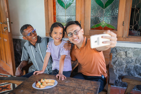 happy asian man taking picture with his father and daughter using phoneの写真素材