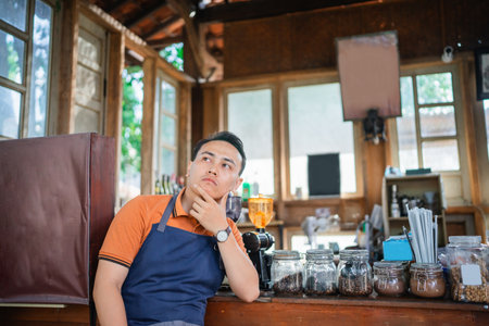 handsome barista in apron waiting customer with hand on chin gestureの写真素材