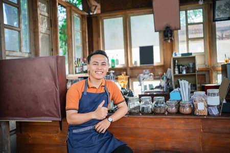asian male barista working in a coffee shop, thumb up hand gestureの写真素材