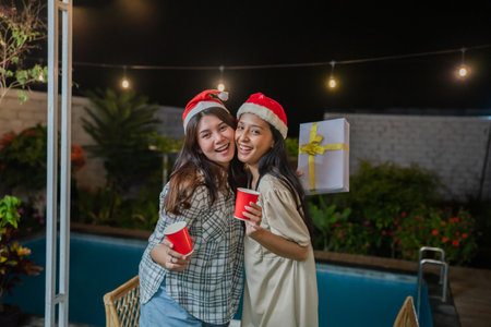 Two friends joyfully celebrate the holiday season in festive attire, holding drinks and laughingの写真素材