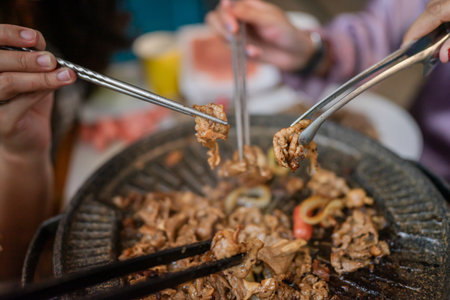Gathered around a grill, friends are savoring and enjoying delicious, perfectly barbecued meatの写真素材