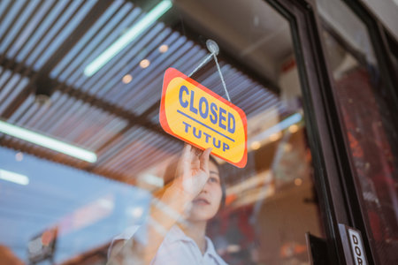 asian female employee flipping closed sign, ending operational hour