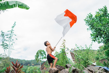 unclothed child raises the Indonesian flag excitedly with nature in the background