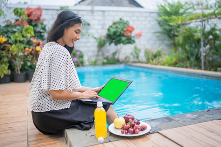 A woman joyfully enjoys her work by the poolside, surrounded by fresh fruits and drinksの写真素材