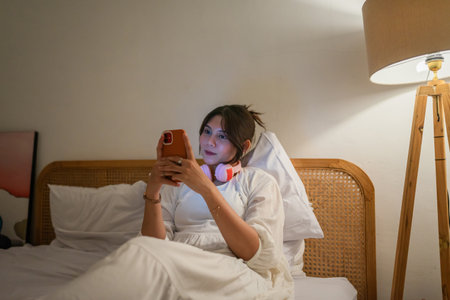 A person is happily relaxing in bed with headphones and a smartphone, enjoying leisure timeの写真素材