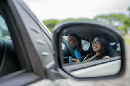A joyful couple smiles together while driving, reflected in the cars side mirrorの写真素材