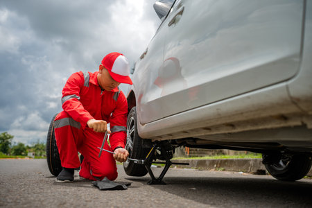 A mechanic in a red uniform is repairing a vehicle on the roadside for safety and efficiencyの写真素材