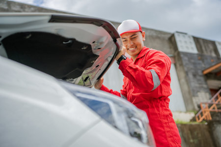 A mechanic is happily inspecting a car engine under the hood of the vehicle outdoorsの写真素材