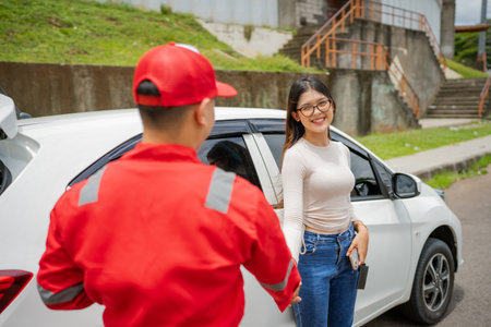 A delivery person greets a happy customer at her car, showcasing quality service.の写真素材
