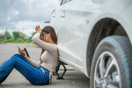 A woman sits next to her car, focused on her phone.の写真素材