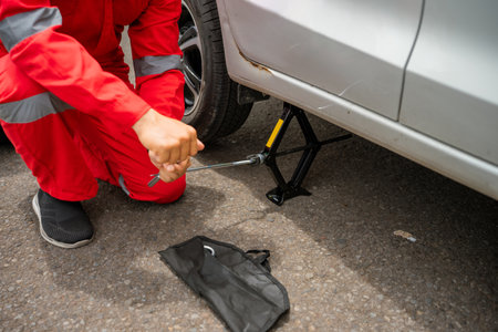 A mechanic using a jack to change a tire on a silver vehicle in an outdoor setting.の写真素材