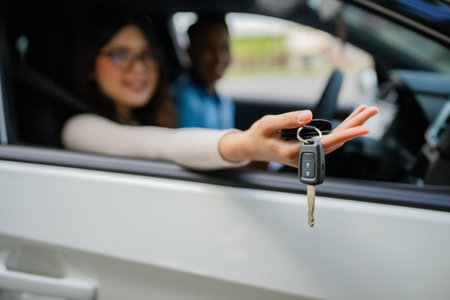 A young woman is handing over the car keys to someone from the drivers seat of a vehicleの写真素材