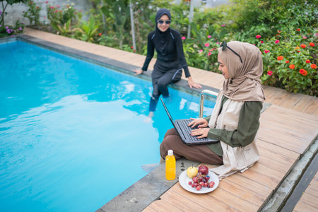 Two women are having a productive day by the pool, working while enjoying relaxationの写真素材